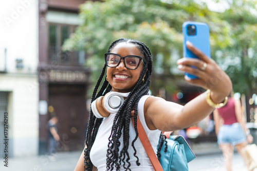 Smiling Latina woman with braided hair on the street using her smartphone