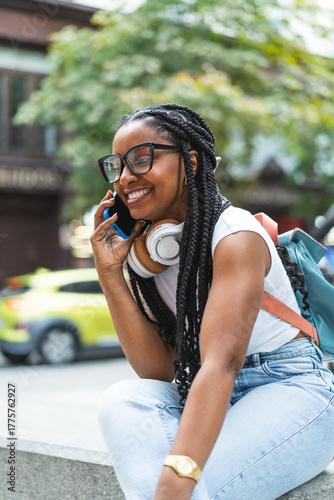 Smiling Latina woman with braided hair standing on the street using her smartphone