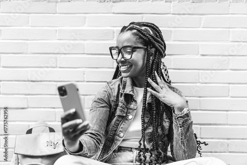 Smiling Latina woman with braided hair Sitting on the street using her smartphone