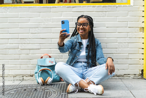 Smiling Latina woman with braided hair Sitting on the street using her smartphone