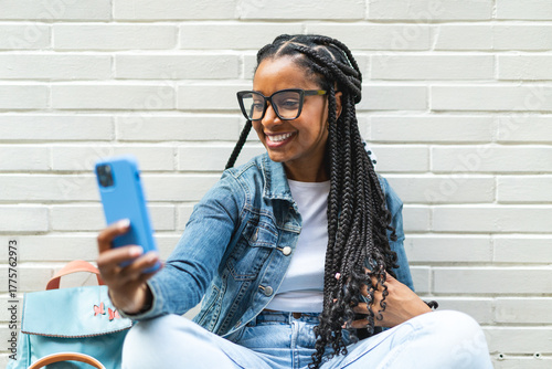 Smiling Latina woman with braided hair Sitting on the street using her smartphone