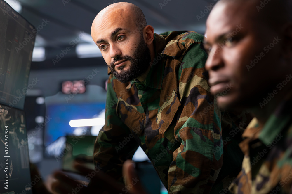 Fototapeta premium Team of military dispatchers looking at surveillance monitor, analyzing data to allocate resources to units based on mission needs. Agent and colleague examining strategic data on equipment displays