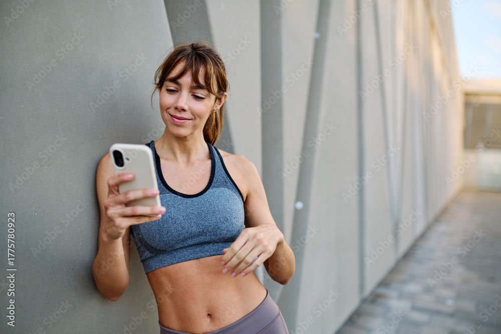 Fototapeta premium Woman in sportswear checks phone while enjoying outdoor fitness activity