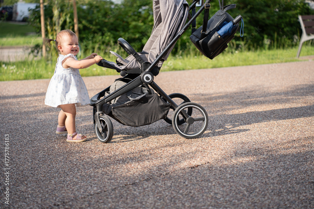 Obraz premium adorable child joyfully pushes a stroller outdoors on a sunny day, surrounded by greenery, capturing a moment of innocent play and exploration, carefree, moment, cherish, family, earth, warmth