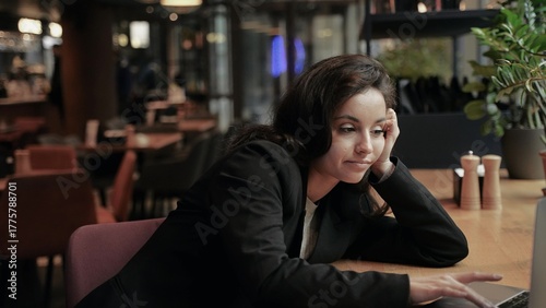 Foto Tired young woman sitting in the restaurant while working on the laptop, leaning on the table