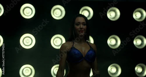 bikini fitness athlete showcases her posing technique on stage under bright lights. The focus is on her confident stance and athletic build as she prepares for the competition.