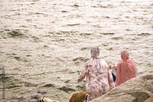Two Iranian women with their heads covered sitting on rocks looking out into the ocean