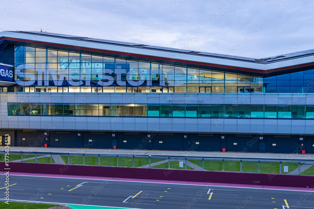 Obraz premium The Silverstone pit building lit up at twilight, ideal for motorsport, travel, and architecture themes.