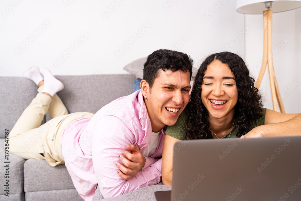 Fototapeta premium Young couple laughing enjoying digital content on laptop