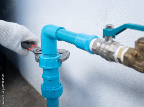 Fotografie Plumber tightening PVC union fitting with pipe wrench on home water pump system