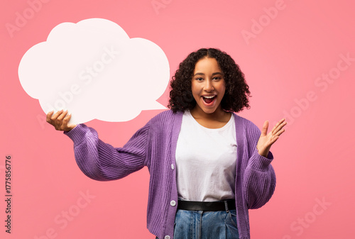 Tablou pe pânză An enthusiastic young black woman is in a pink studio, joyfully holding an empty speech bubble while expressing her excitement