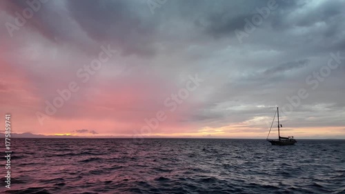 A magnificent sunset while sailing on the Aegean Sea. A sailboat sails in the distance.