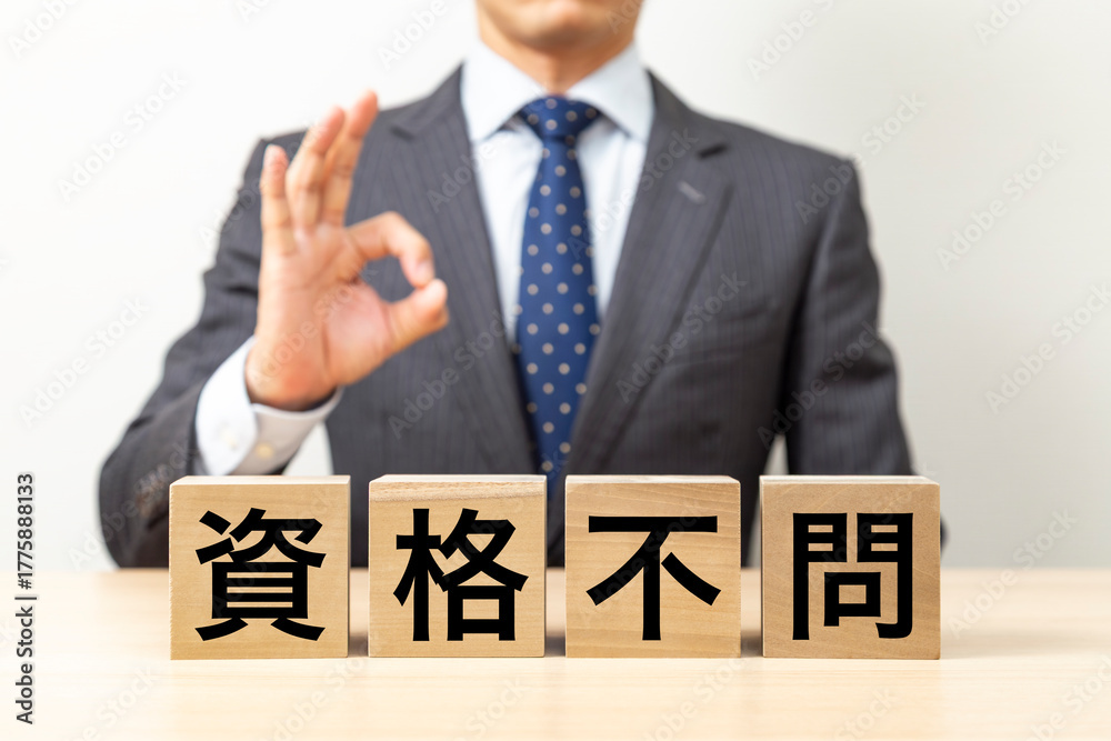 Obraz premium 「資格不問」と書かれたブロックとOKポーズをするビジネスマン