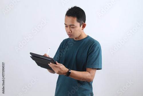 Focused Asian man drawing or writing on a digital tablet with a stylus pen.