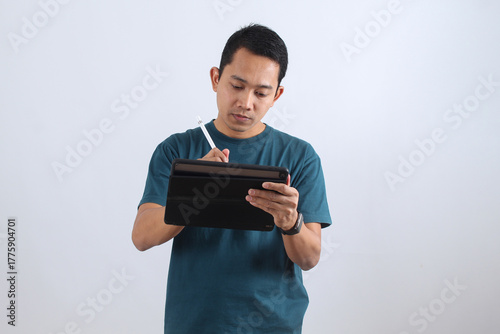 Focused Asian man working on digital tablet with stylus pen