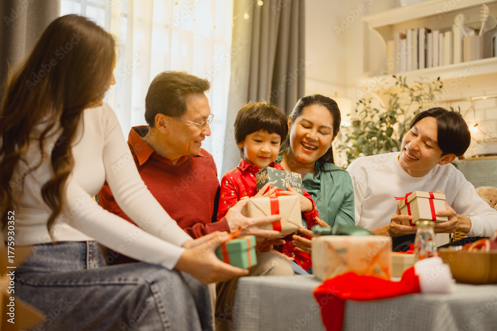 Obraz premium family, christmas, happy family, families, Asian family exchanging Christmas gifts together at home, sharing love, laughter, and joyful moments in a warm and festive holiday atmosphere.