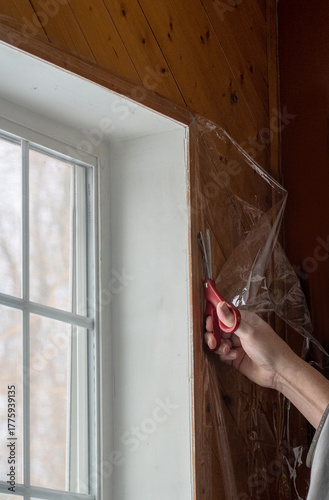  a hand holding scissors is Trimming window  plastic, used for window insulation and saving on the heating bill in winter 