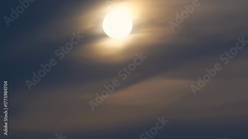 Bright orb in a hazy sky. Clouds obscure the sun, casting gentle light and shadows