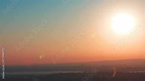 A hazy sunset over a cityscape and water, with a bright sun, gradients