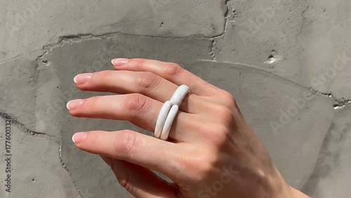 close-up photograph of a feminine hand showcasing a simple white silicone band wedding ring positioned on a textured gray concrete