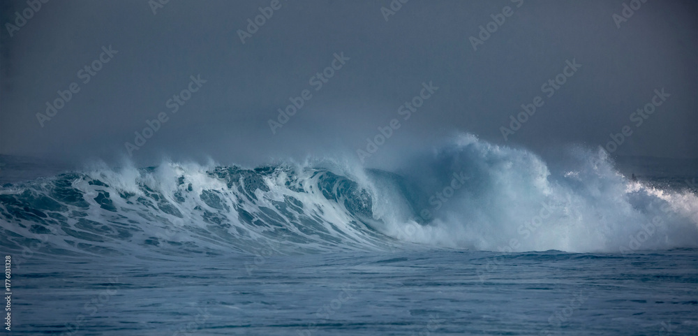 Naklejka premium Hawaii, Oahu island at Northshore, sunrise lit big surfing crashing ocean wave with dark mist on horizon line with copyspace