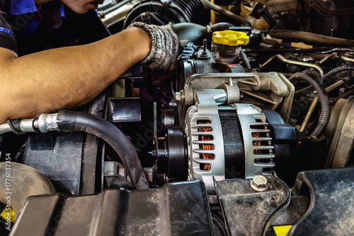 Close up to alternator or electrical generator under the hood of pick up car with blurred image of mechanics inspect and repair in background. Old aluminum mud pulley car generator for repair.