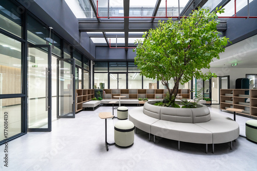 bright atrium with a large tree, modern seating, and glass roof, creating a vibrant indoor garden space
