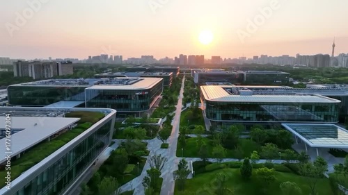 Aerial view of a modern corporate campus with sleek glass buildings and lush green landscaping at sunset.