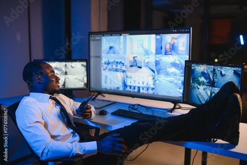 African American security officer or dispatch uses computer and walkie talkie, looks at screens