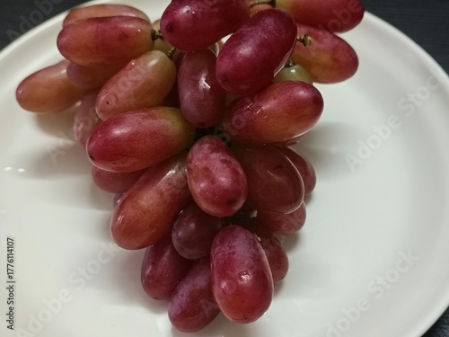 A bunch of fresh red grapes on a white plate, perfect for healthy food concepts, diet menus, natural fruit photography, and nutrition or wellness advertising designs.