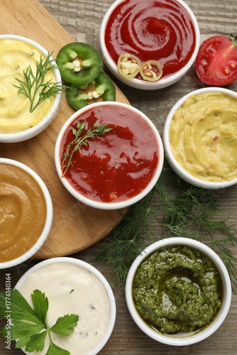Different sauces and herbs on wooden table, flat lay