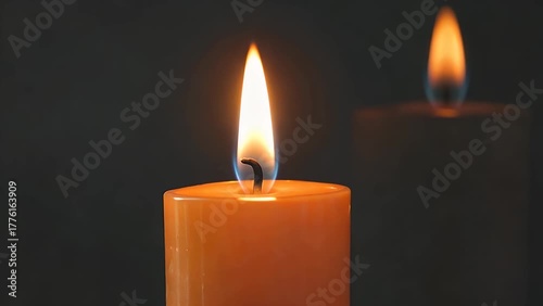 detailed close-up photograph of the bright flame burning on top of an orange-colored wax candle against a dark