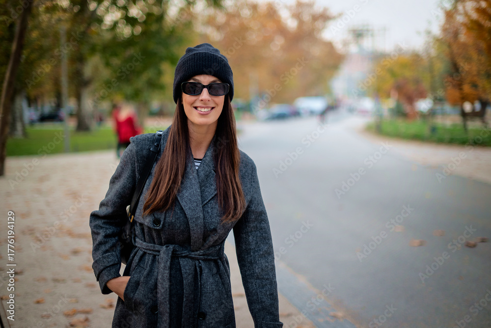 Fototapeta premium Smiling middle-aged woman wearing scarf and beanie in a park during the autumn season