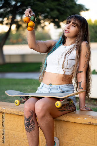 Tattooed woman sitting with skateboard holding tangerines