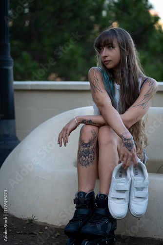 Tattooed woman sitting wearing inline skates holding shoes