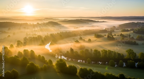 Golden light filters through ethereal morning mist, illuminating a tranquil river winding through a lush, forested valley at sunrise, creating a breathtaking aerial landscape vista