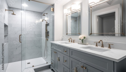 An elegant, remodeled bathroom with a grey vanity and bronze hardware. The shower has a large shower head and marble tiles and glass wall line the sides
