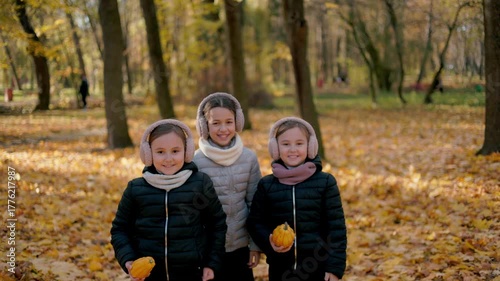 The sisters are playing with leaves in the park and smiling.The children dance to the beat, smile, and it seems that their energy and music add even more bright colors to this wonderful autumn day.