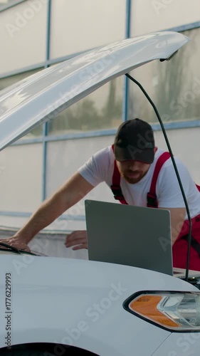 Mechanic inspecting vehicle performance data on laptop while working on car engine, showcasing automotive expertise and attention to detail in a professional environment
