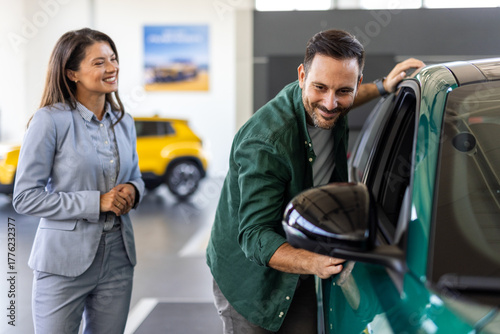 Happy middle age businessman buying new and luxury car. Beautiful female dealer helps him to make right decision.
