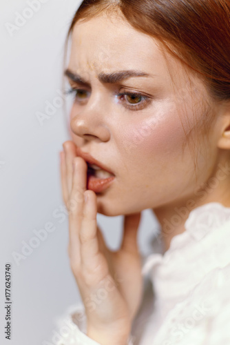 Concerned young woman expressing anxiety about hair loss with a worried expression, dressed in a casual white top, captured in soft pastel tones against a neutral background