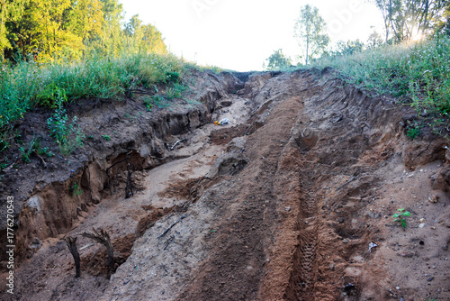 Steep sandy slope deeply eroded by rain. Fresh motorcycle tracks ascend the raw, rugged terrain, showcasing natural forces and off-road adventure