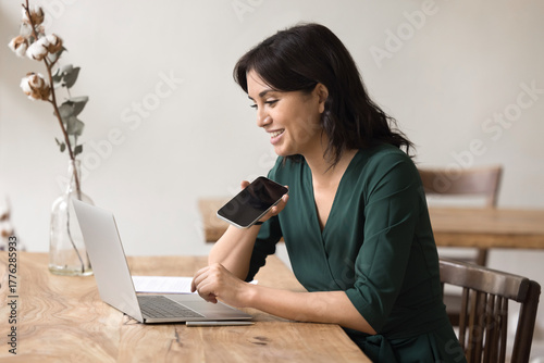 Canvas-taulu Young female working on notebook dictating audio notes using phone