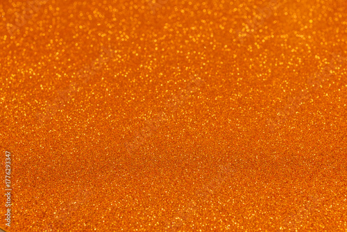 Orange glitter background with golden sparkles in sharp focus at bottom, shimmering grains create radiant festive effect blending softly into blur above