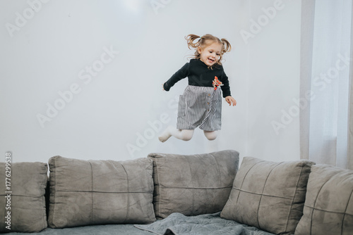 Obraz na plátně A cheerful young child leaps joyfully on a cozy sofa in a well-lit home