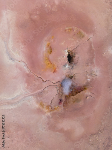 Aerial view of a surreal landscape of pink hues and swirling patterns punctuated by dark voids and delicate fractures, Geothermal Areas, Iceland.