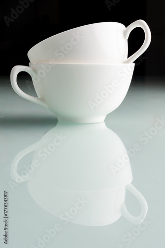 two stacked coffee mugs on blue table with black background and reflection