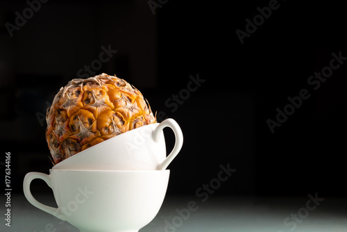 pineapple sitting in  stack of white coffee mugs isolated
