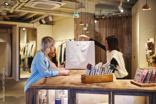 Shop assistant handing shopping bag to smiling customers in boutique