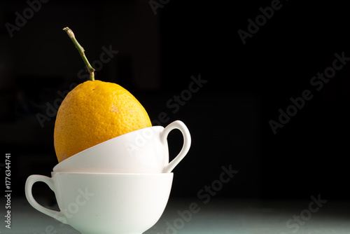 lemon sitting in  stack of white coffee mugs isolated